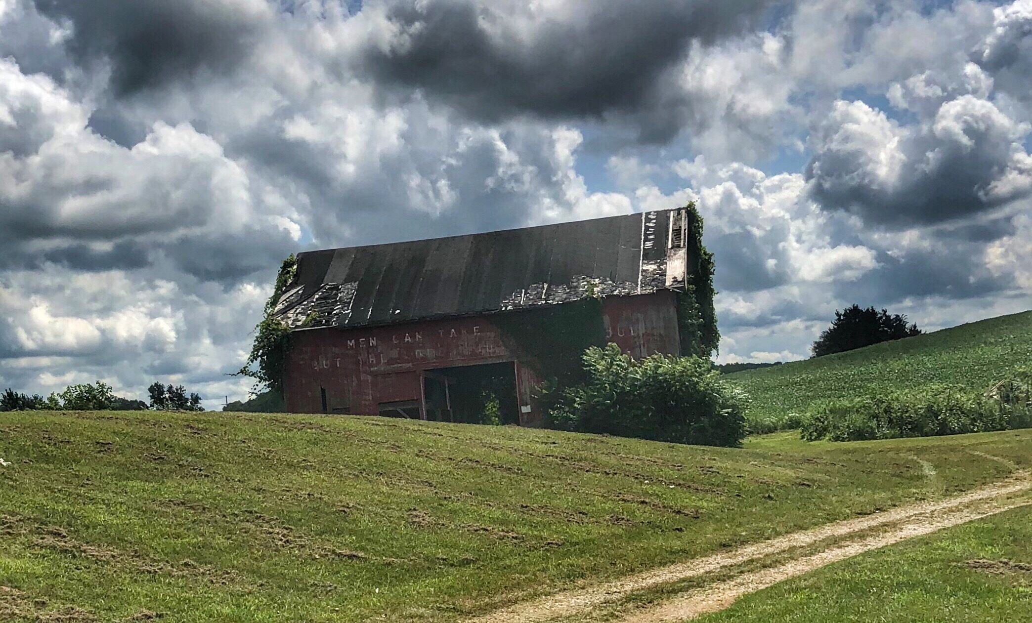 A dilapidated barn on a grassy hill under a cloudy sky.