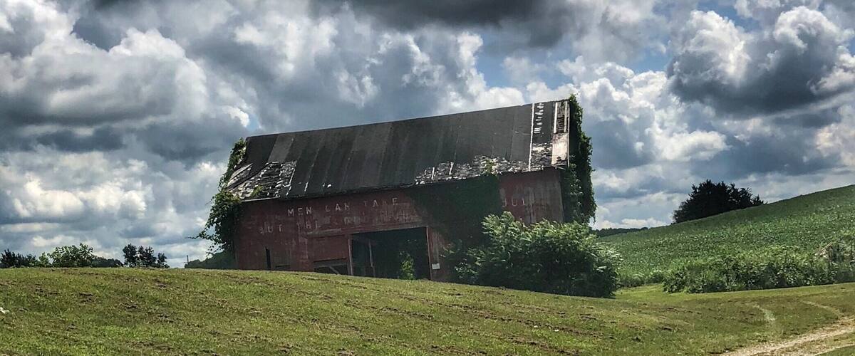 A dilapidated barn on a grassy hill under a cloudy sky.