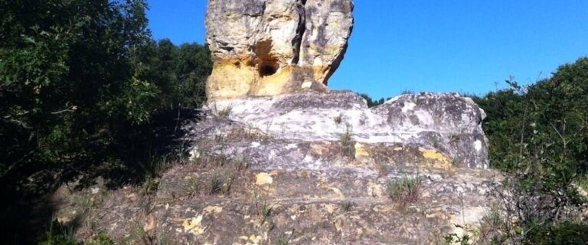 A large rock formation with a cave-like opening, surrounded by trees and vegetation.