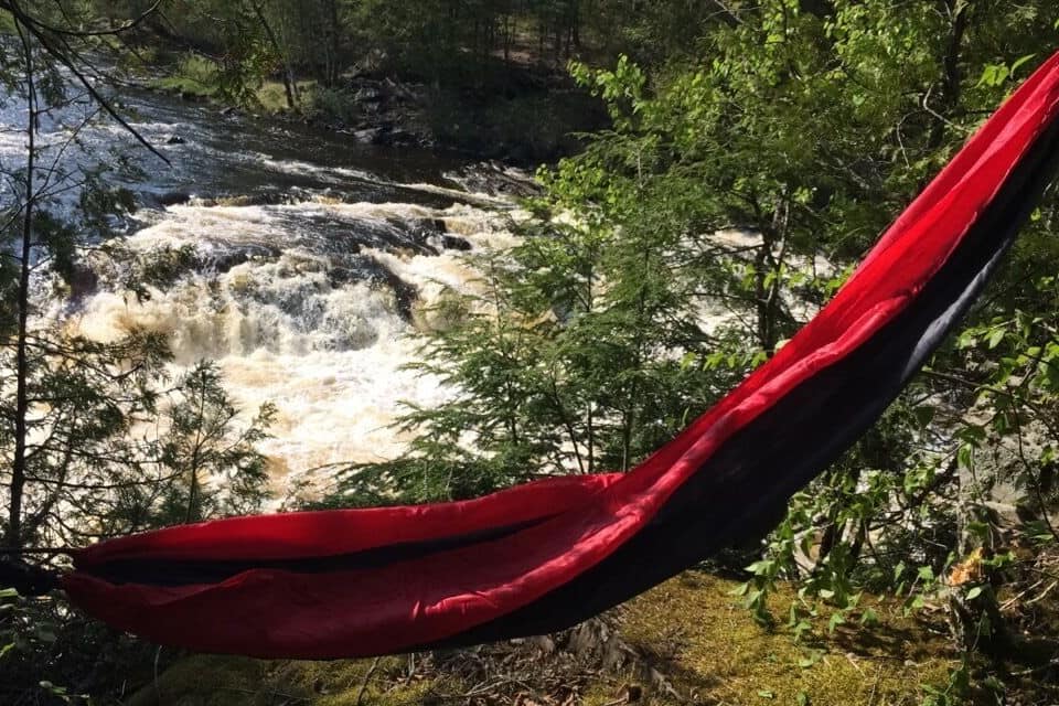 A red hammock in a forest with a rushing river in the background.