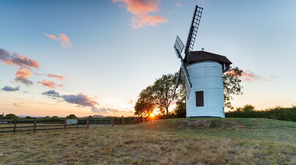 Un molino con cuerpo blanco y techo oscuro, al atardecer con nubes.