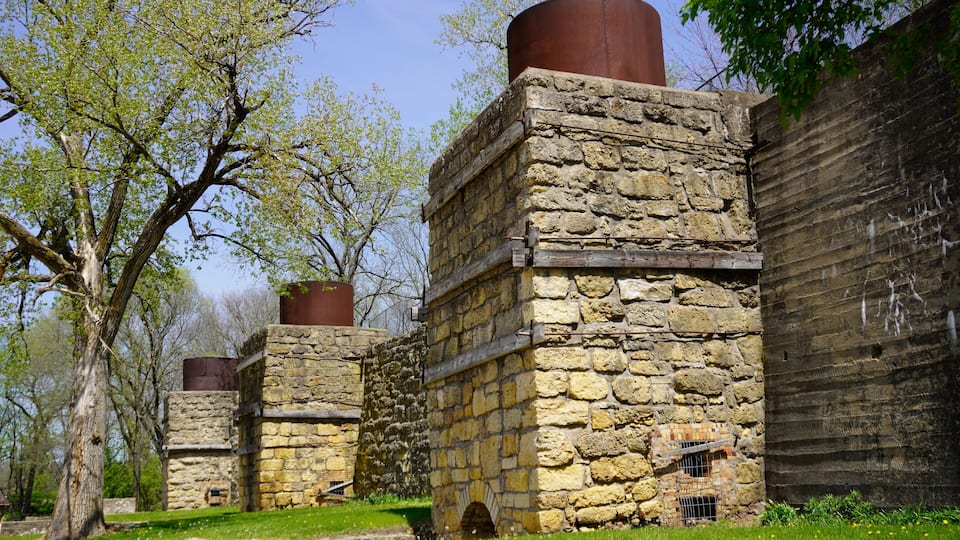 A stone building with a cylindrical chimney, surrounded by trees and grass.