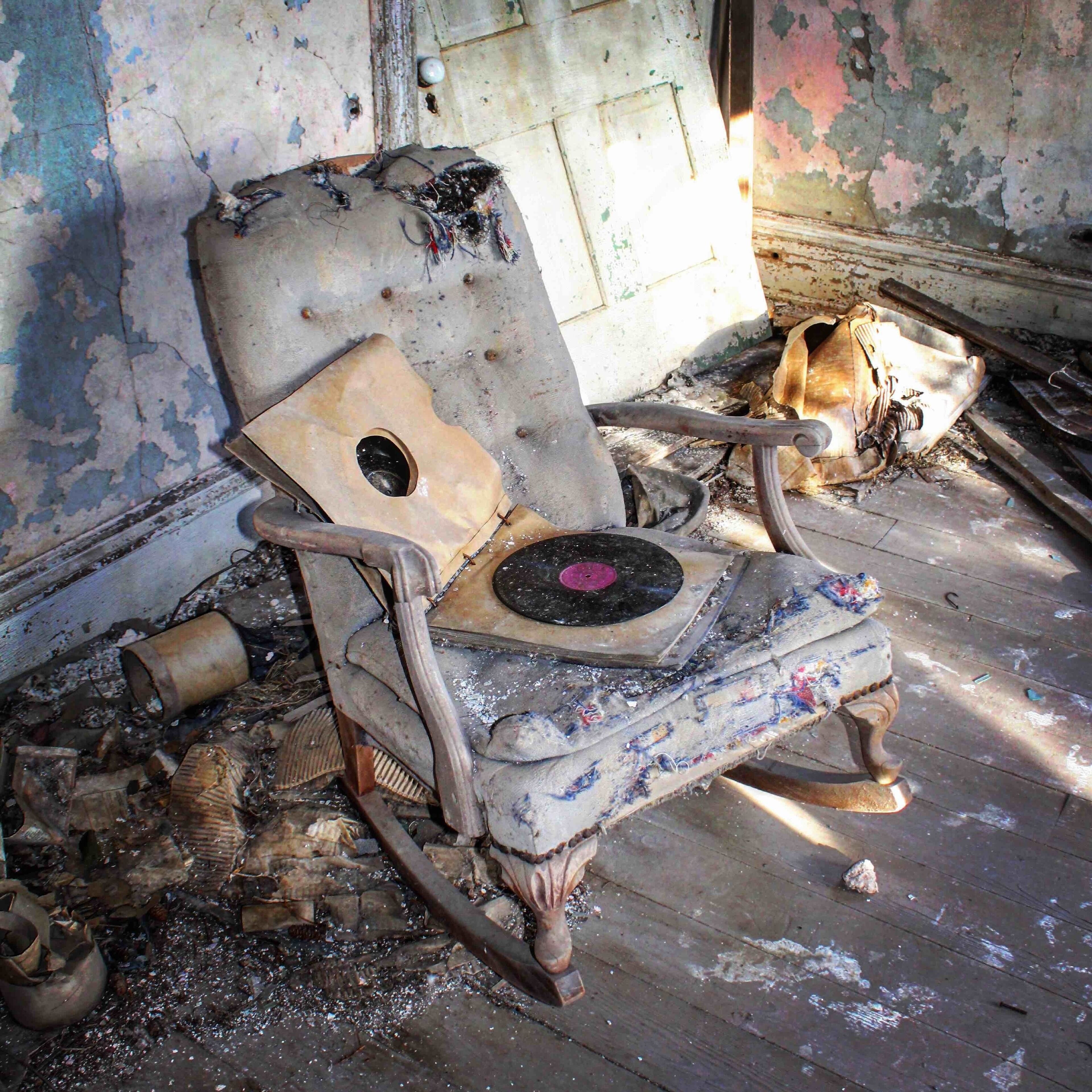 A dilapidated rocking chair in a decayed room with peeling paint and debris.