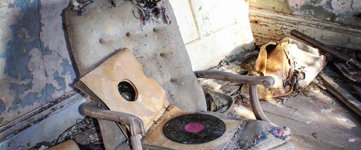 A dilapidated rocking chair in a decayed room with peeling paint and debris.
