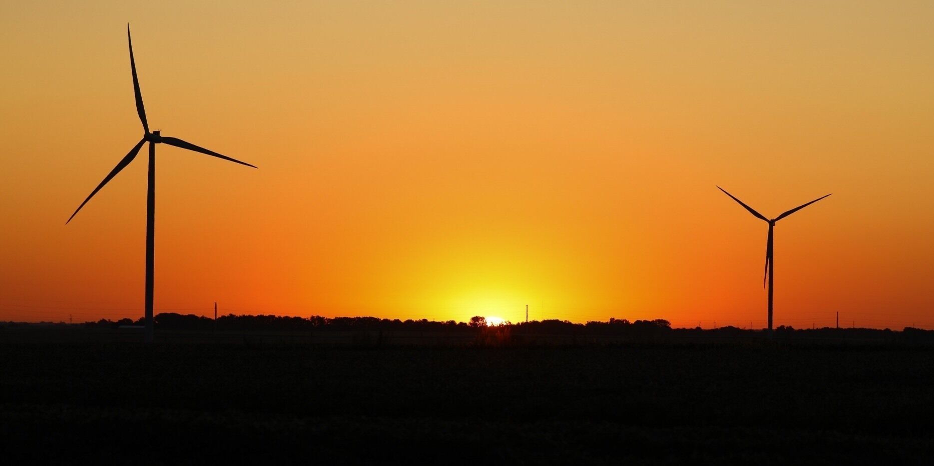 A sunset with two wind turbines silhouetted against the sky.