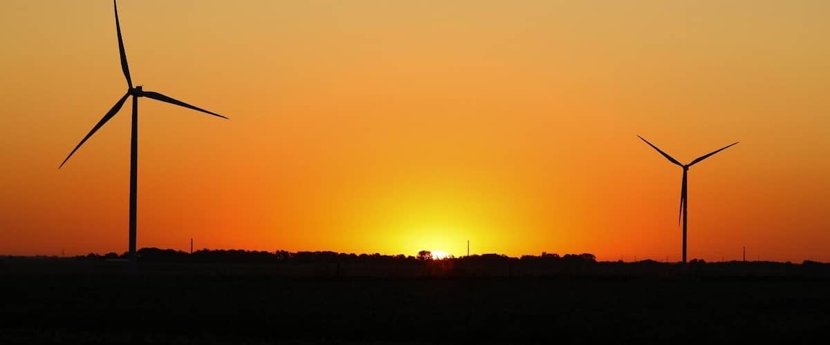 A sunset with two wind turbines silhouetted against the sky.