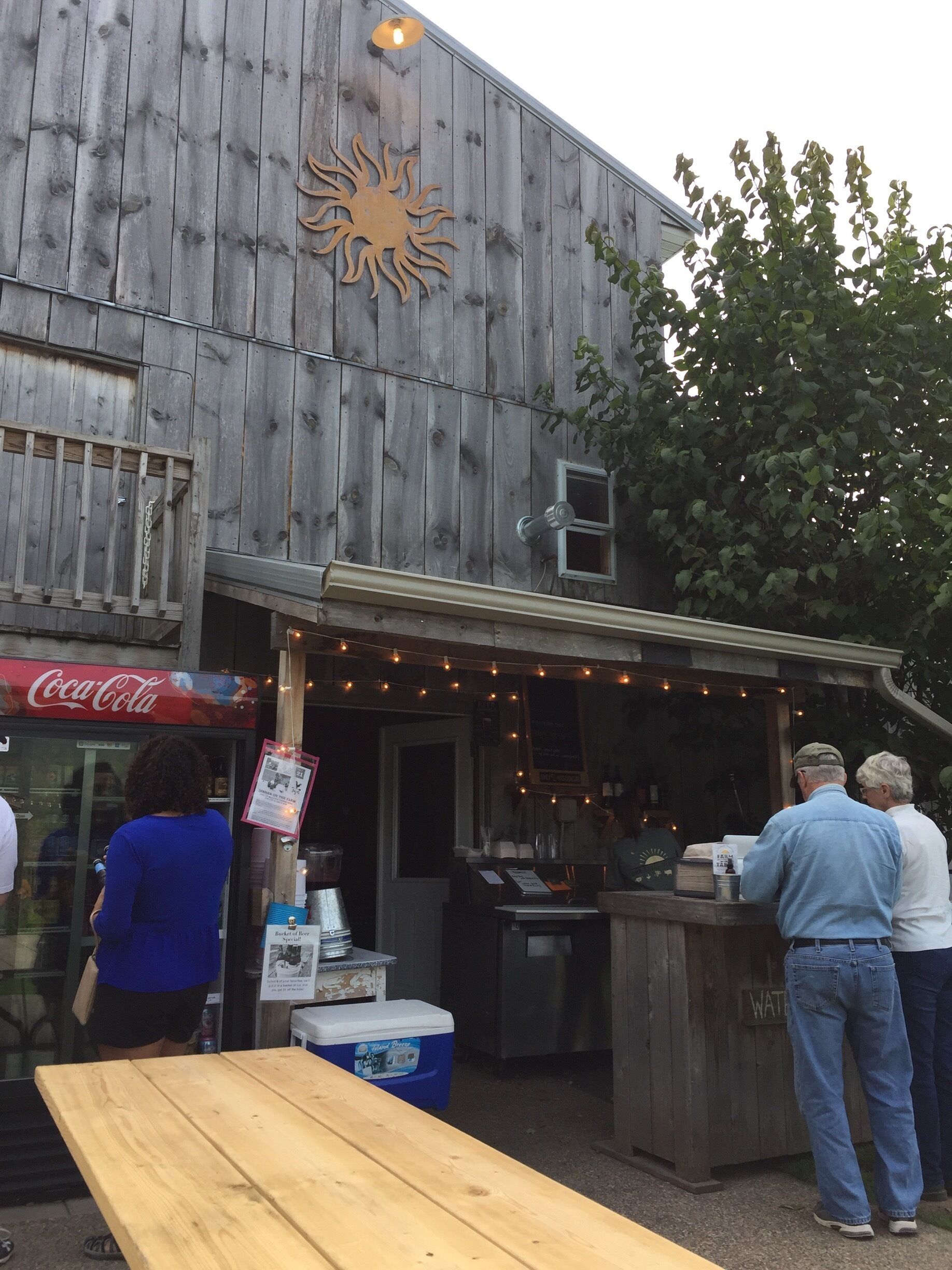 A wooden building with a Coca-Cola sign, a sun decoration, and a wooden table outside.