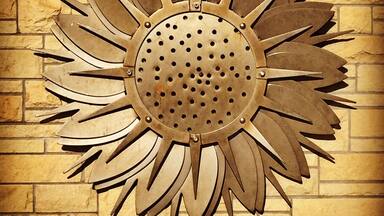 A metal sun decoration with petals on a brick wall.
