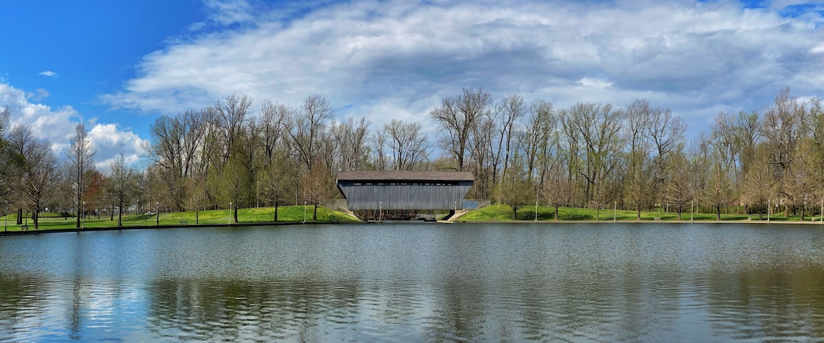 Brownsville Bridge a covered bridge in Columbus, Indiana. Looking across the Mill Race Pond on a clear spring day with blue sky and clouds.