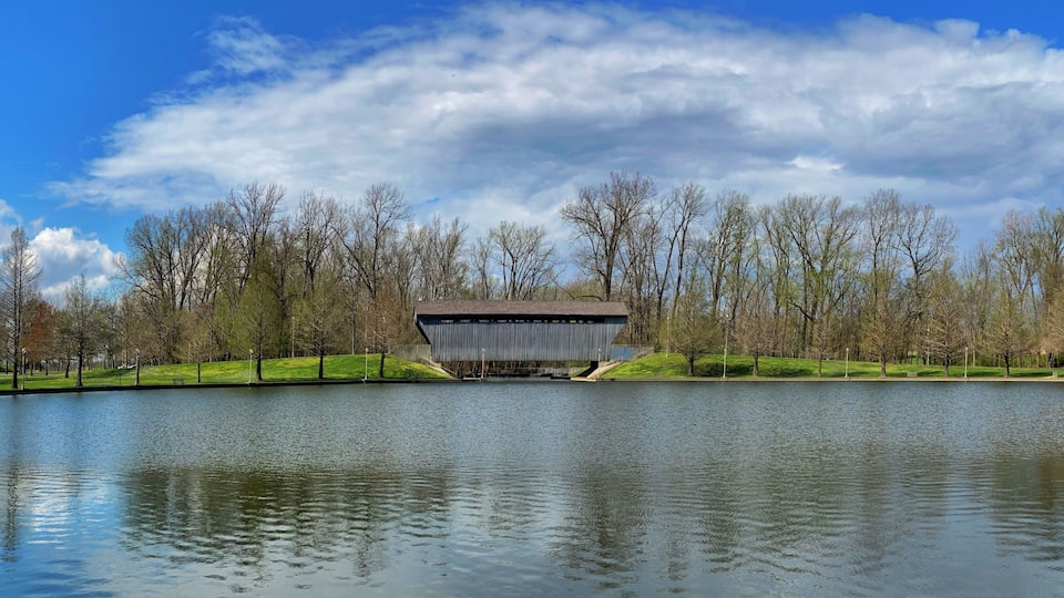 Brownsville Bridge a covered bridge in Columbus, Indiana. Looking across the Mill Race Pond on a clear spring day with blue sky and clouds.
