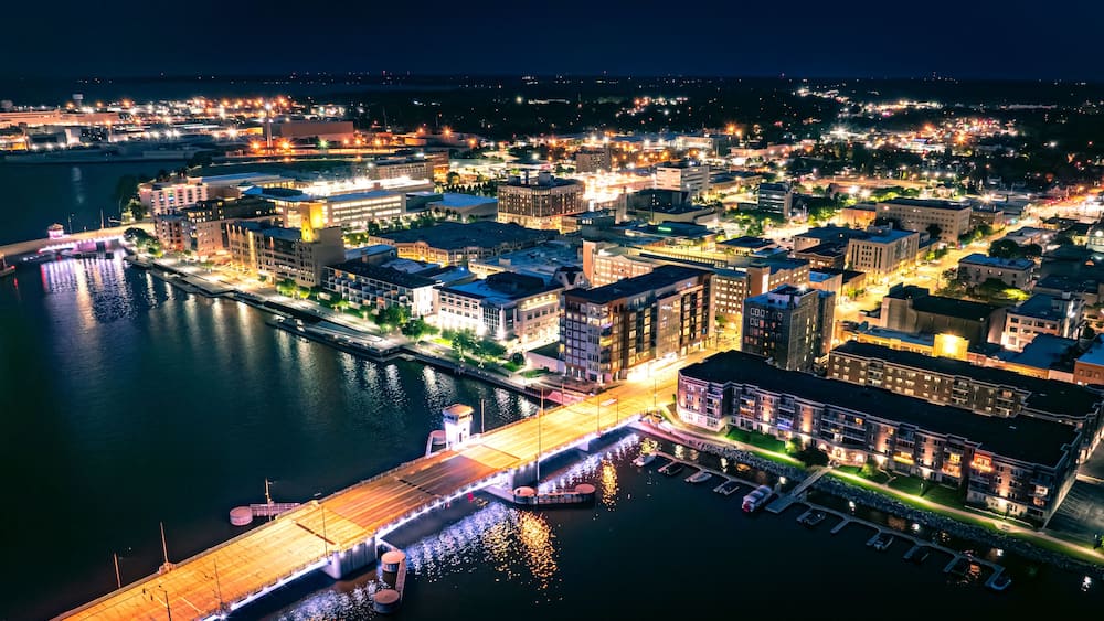 A nighttime cityscape with a waterfront, illuminated buildings, and a bridge.