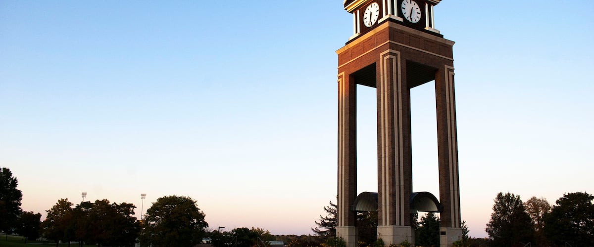 A clock tower with a dome roof and two clocks, surrounded by a landscaped park with trees and a pathway.