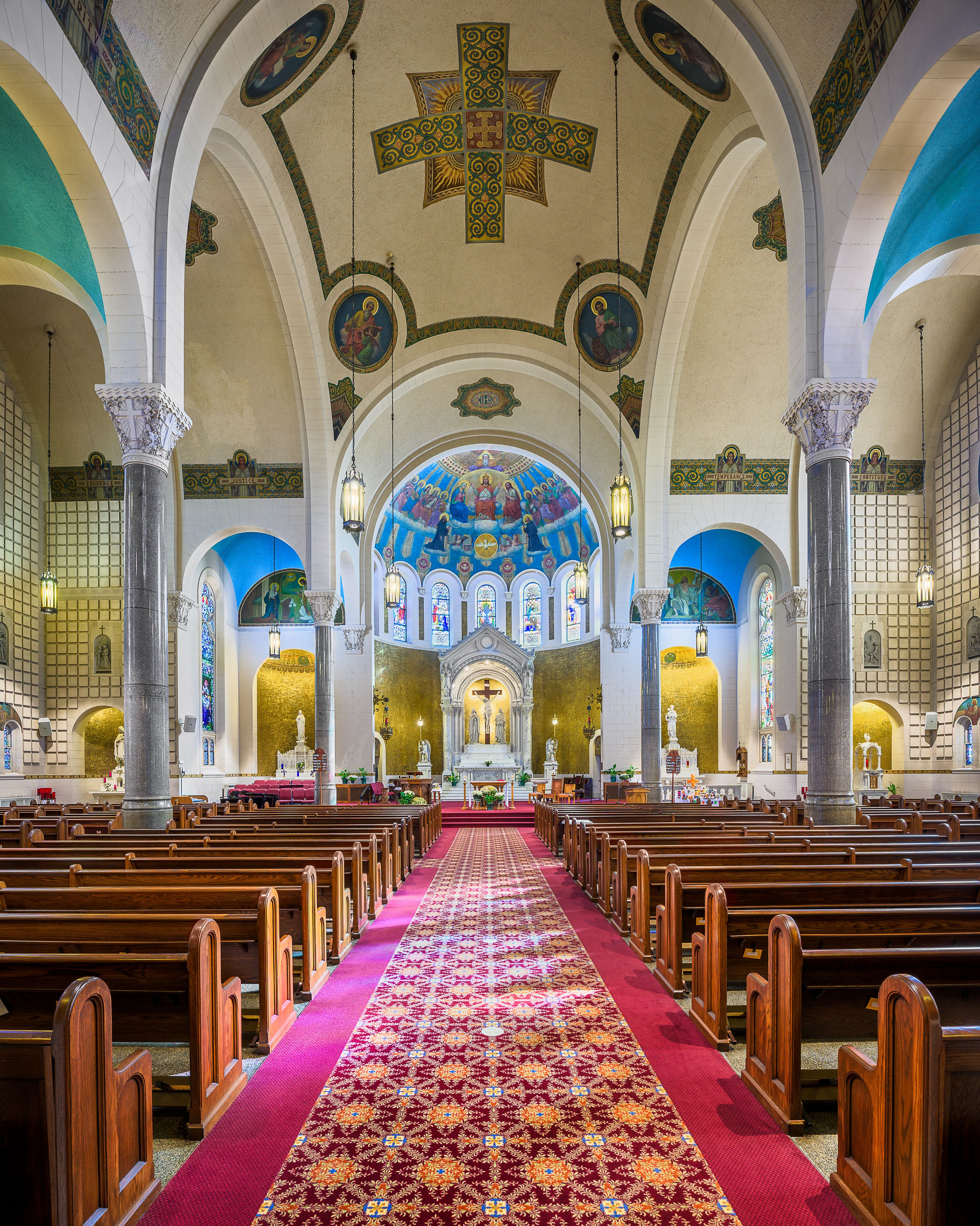 A church interior with wooden pews, a red carpet, and a blue stained glass ceiling.