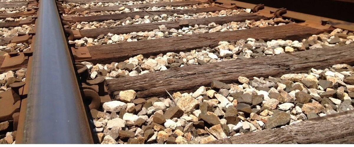 A railway track with gravel ballast and wooden sleepers, surrounded by dense green foliage.