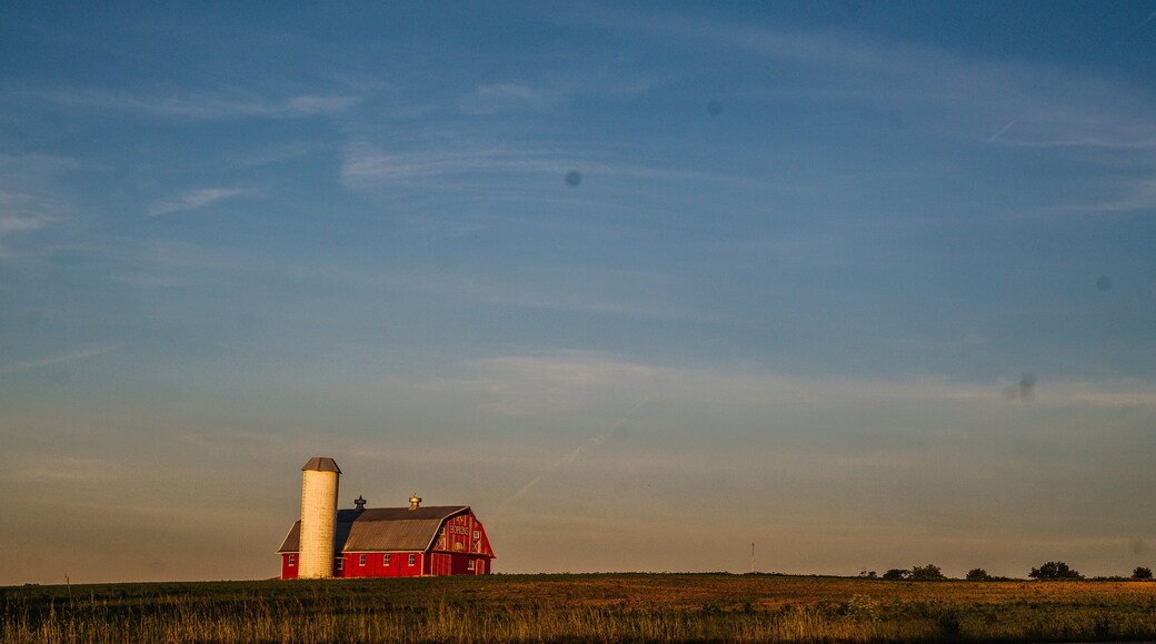A red barn with a silo, set in a vast open field under a clear sky.