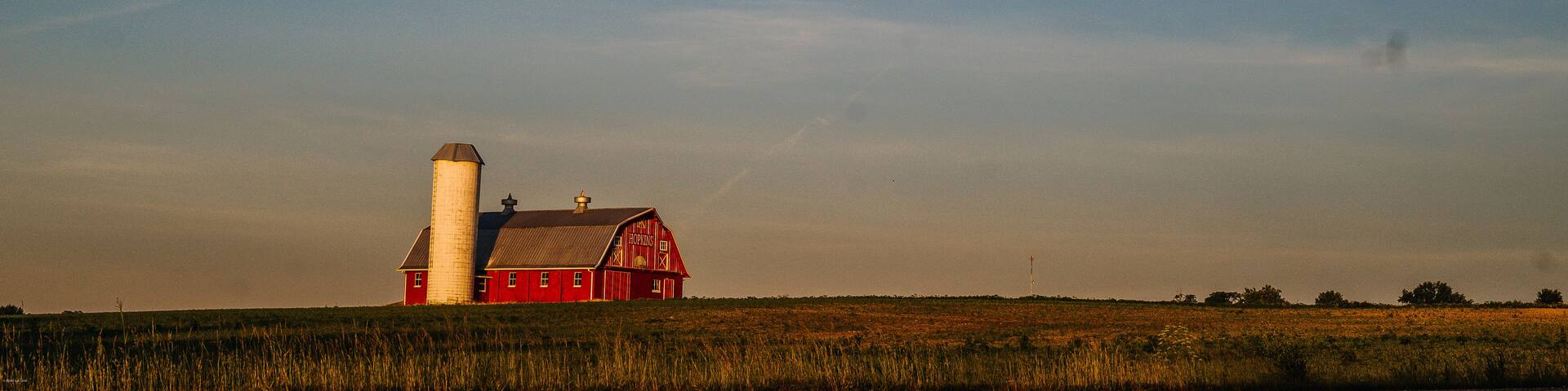A red barn with a silo, set in a vast open field under a clear sky.