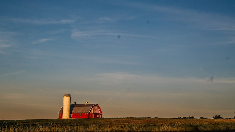 A red barn with a silo, set in a vast open field under a clear sky.