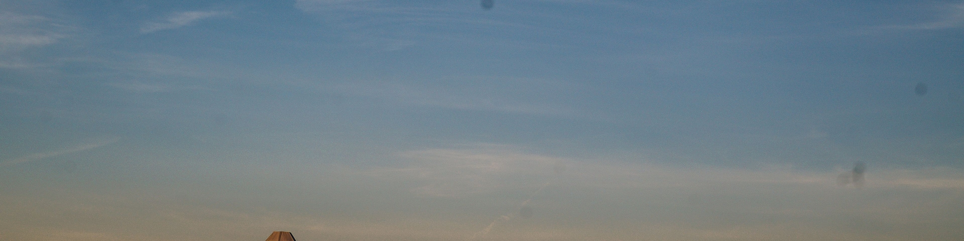 Un granero rojo con un silo, ubicado en un extenso campo abierto bajo un cielo despejado.