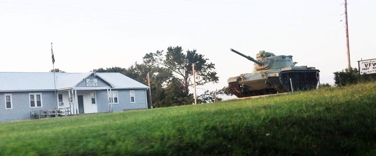 A tank on a grassy hill with a house in the foreground.
