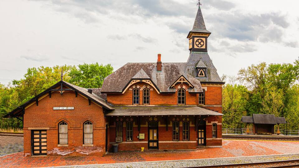 A historic brick train station with a clock tower and a covered waiting area.