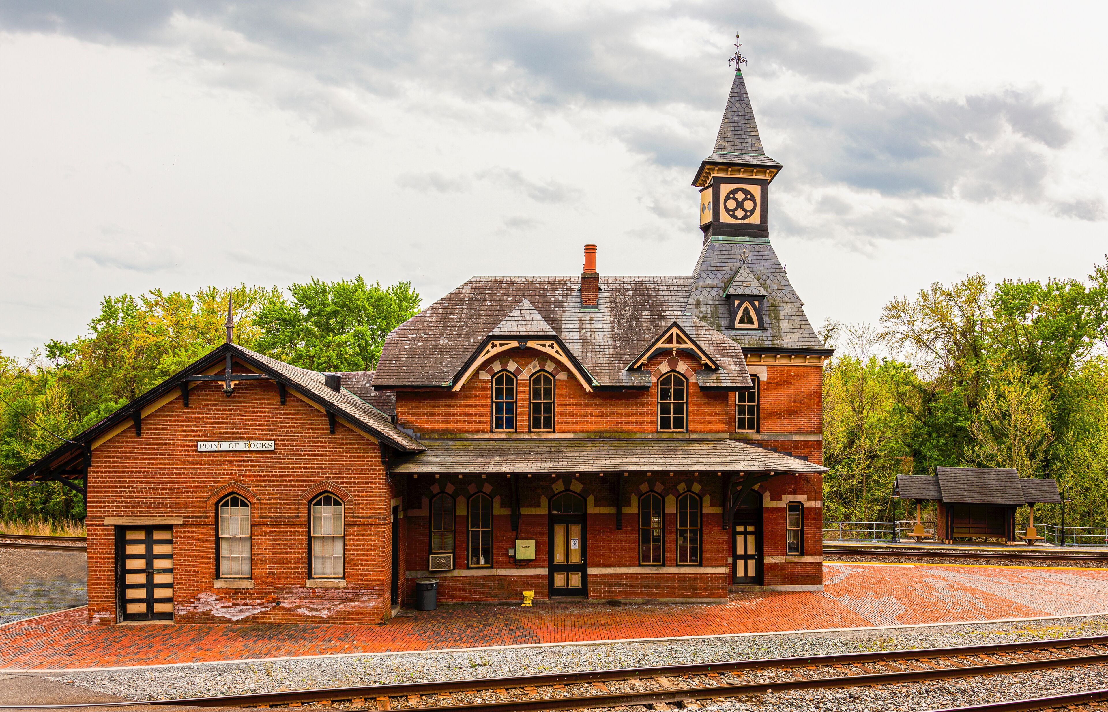 A historic brick train station with a clock tower and a covered waiting area.