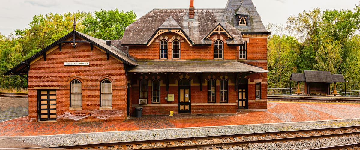 A historic brick train station with a clock tower and a covered waiting area.