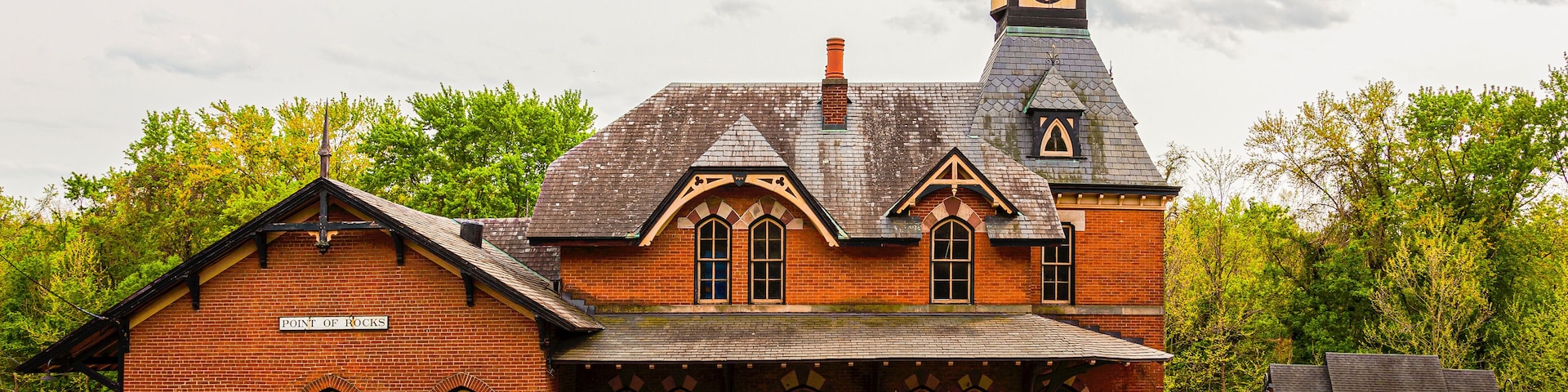 A historic brick train station with a clock tower and a covered waiting area.