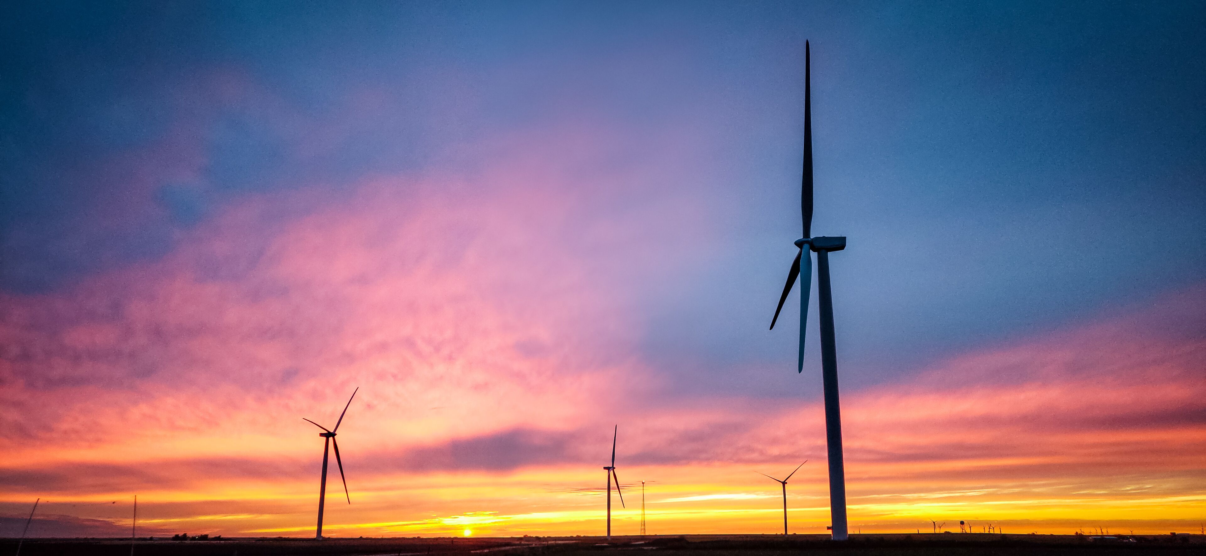 Wind turbines silhouetted against a sunset sky.