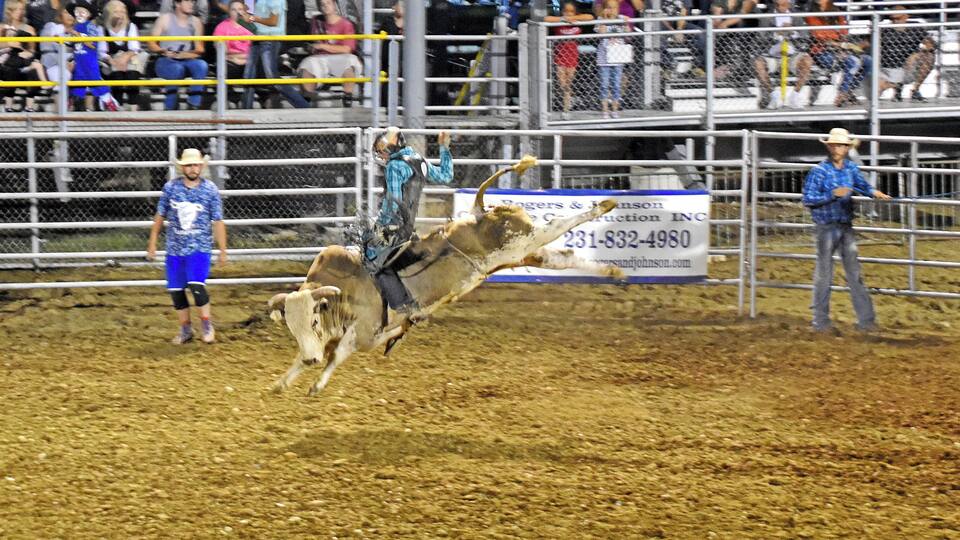 A rodeo event with a bull rider in mid-air, a spectator area, and a fence.