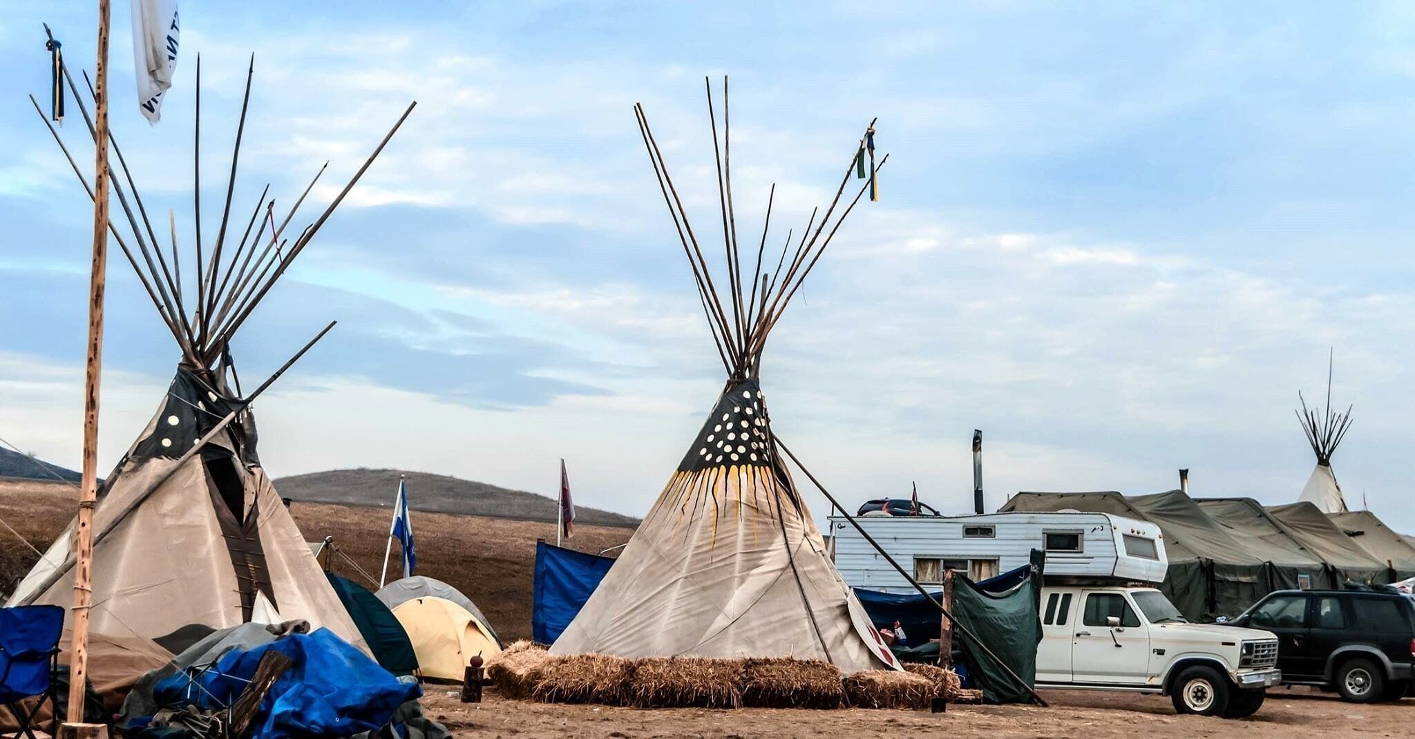 Three tipi tents, a white truck, and a blue tent in a rural setting.