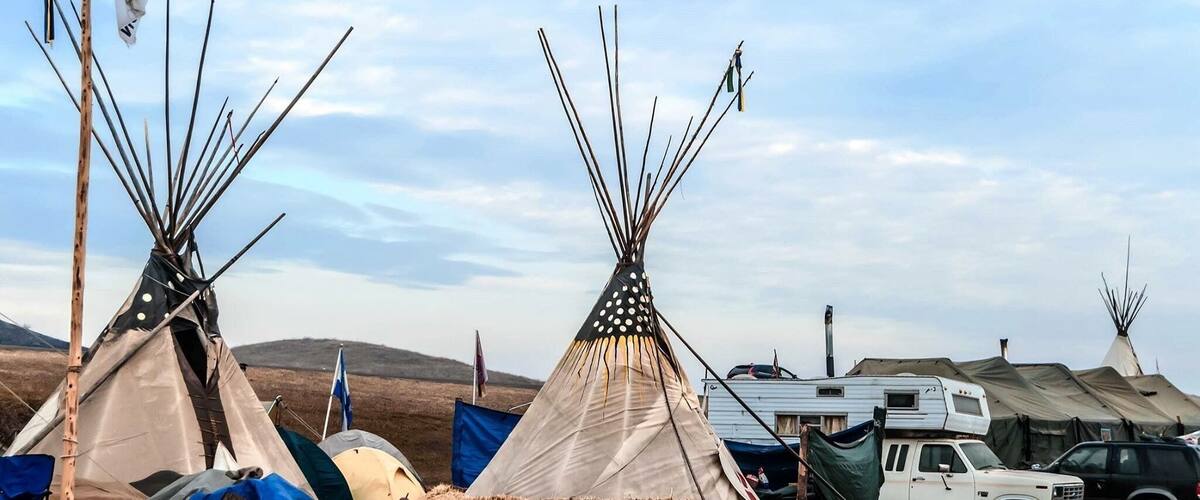 Three tipi tents, a white truck, and a blue tent in a rural setting.