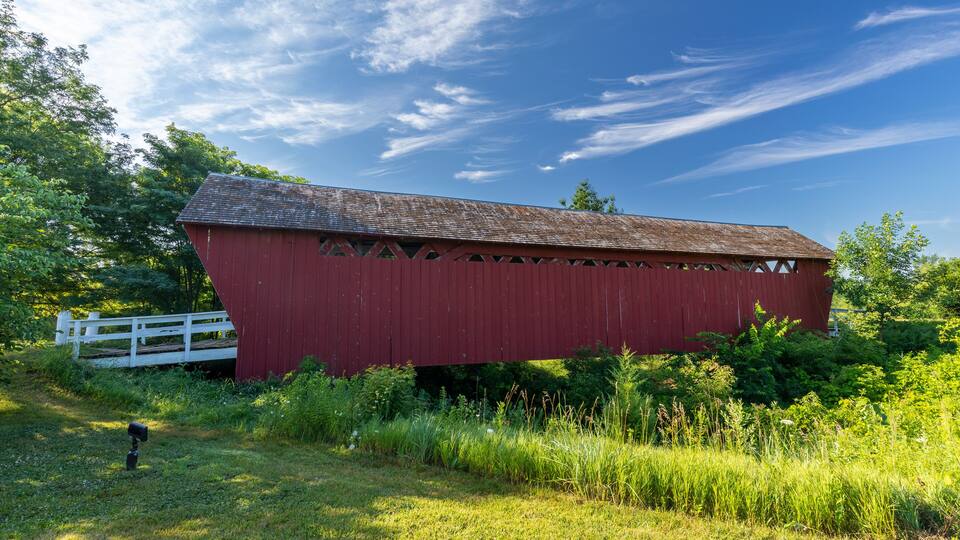 A red covered bridge with a white fence in the background.