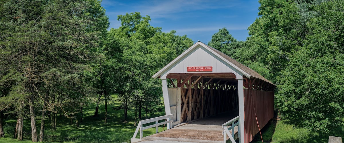A covered bridge with a sign reading "GUTLER-DONAHUE BRIDGE Built 1870" in a forested area.