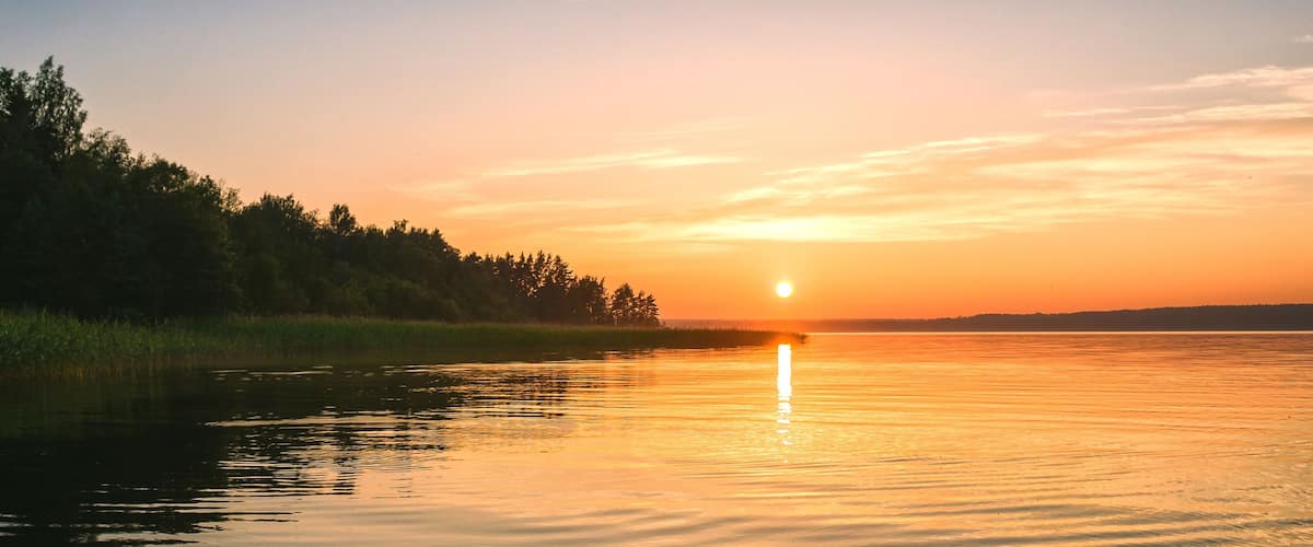 A sunset over a calm lake with trees on the left and a clear sky.