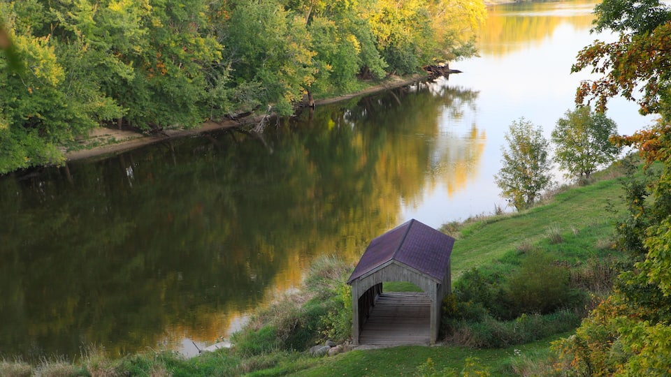 A wooden structure near a calm lake surrounded by lush greenery.