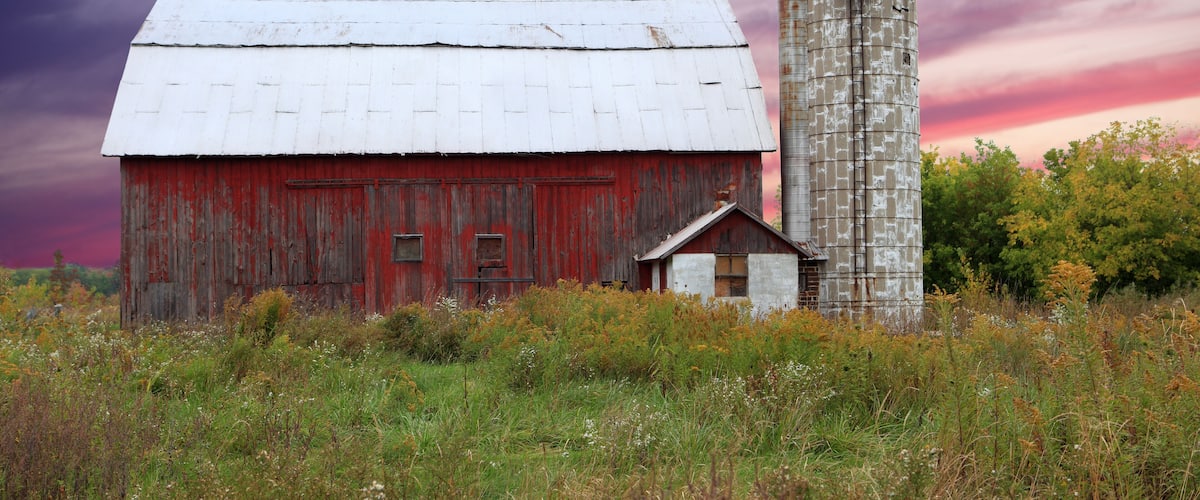 A red barn with a silo in a field.