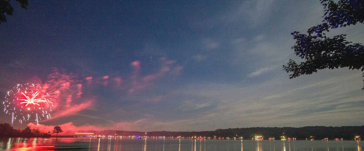 A night sky with fireworks over a calm lake, reflecting city lights on the water.