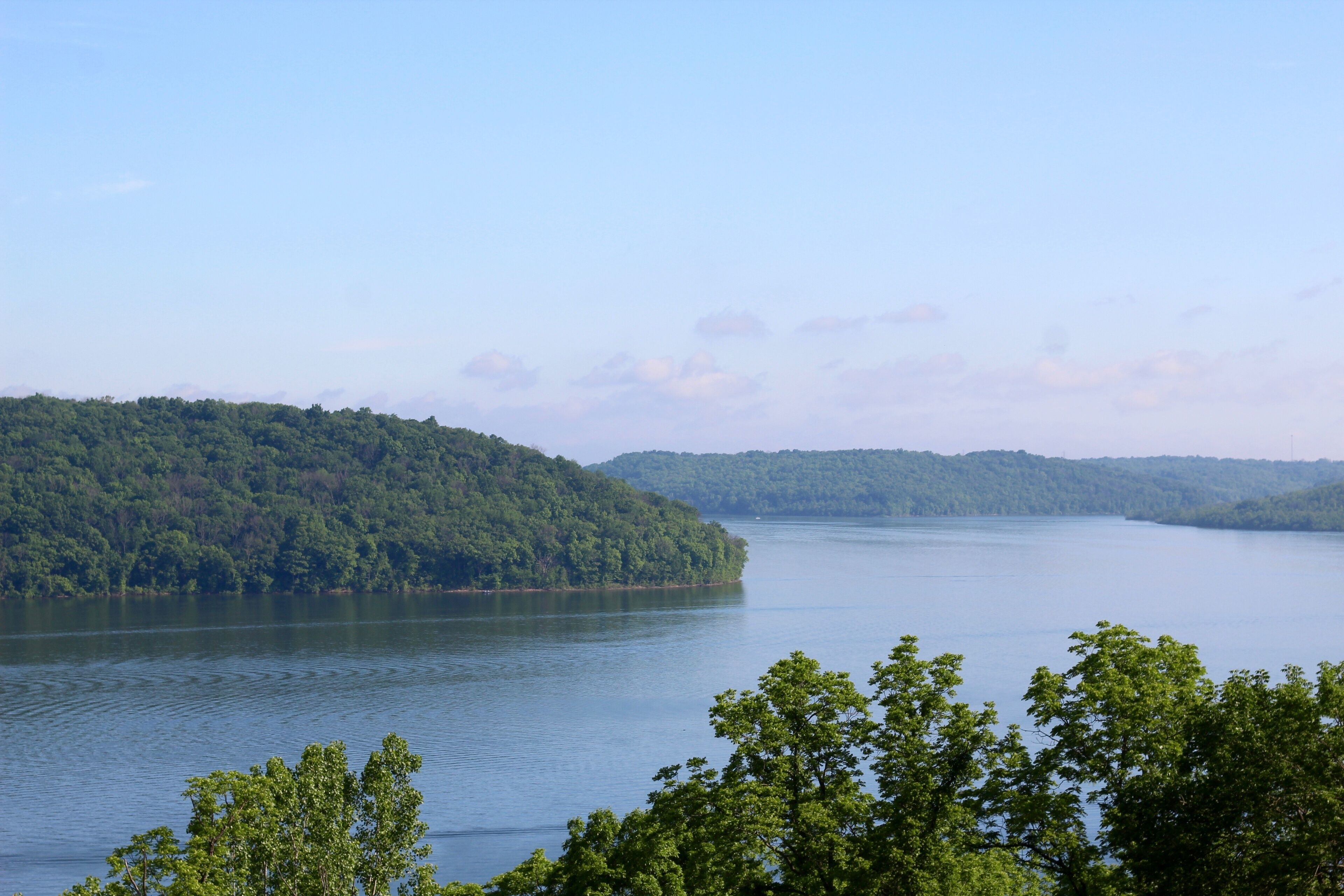 A calm lake surrounded by dense green forest and hills.