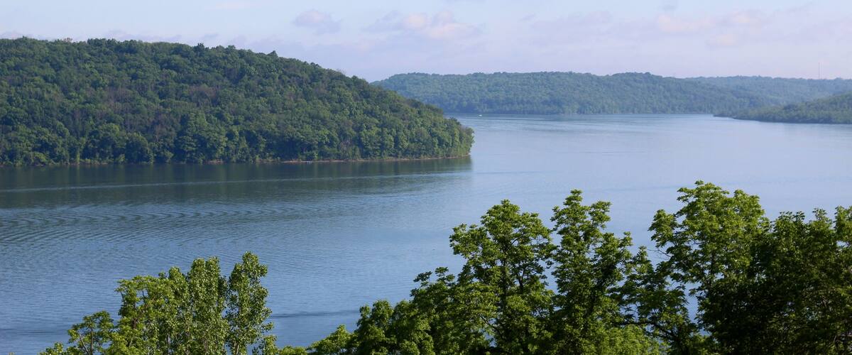 A calm lake surrounded by dense green forest and hills.