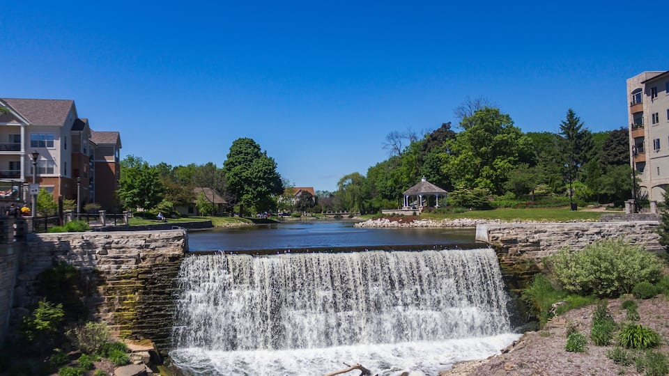 A waterfall cascading into a river, surrounded by greenery and buildings.