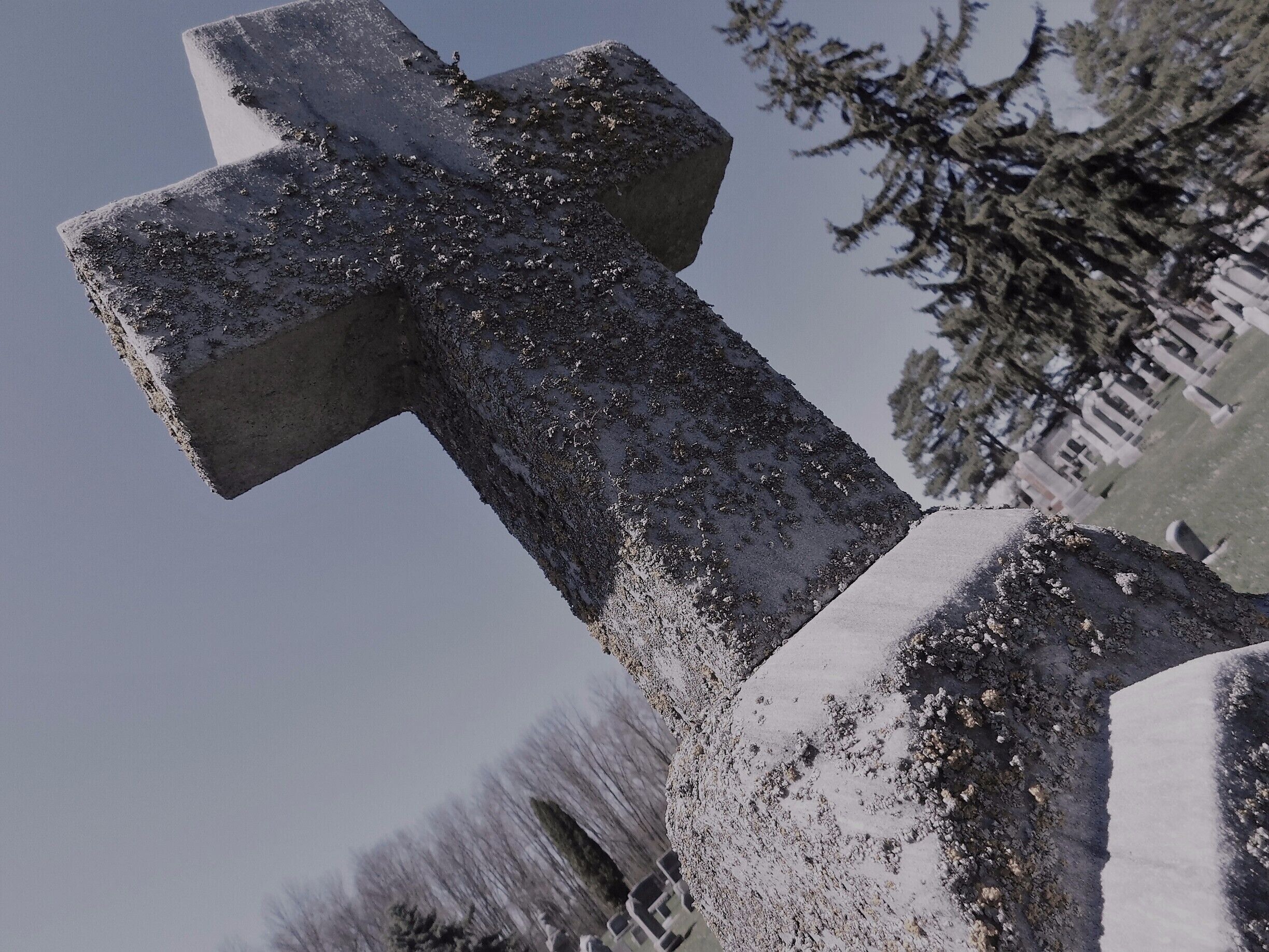 A stone cross covered in snow, with a cemetery in the background.