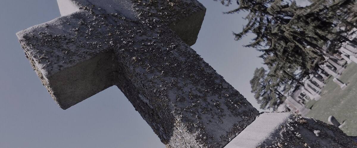 A stone cross covered in snow, with a cemetery in the background.