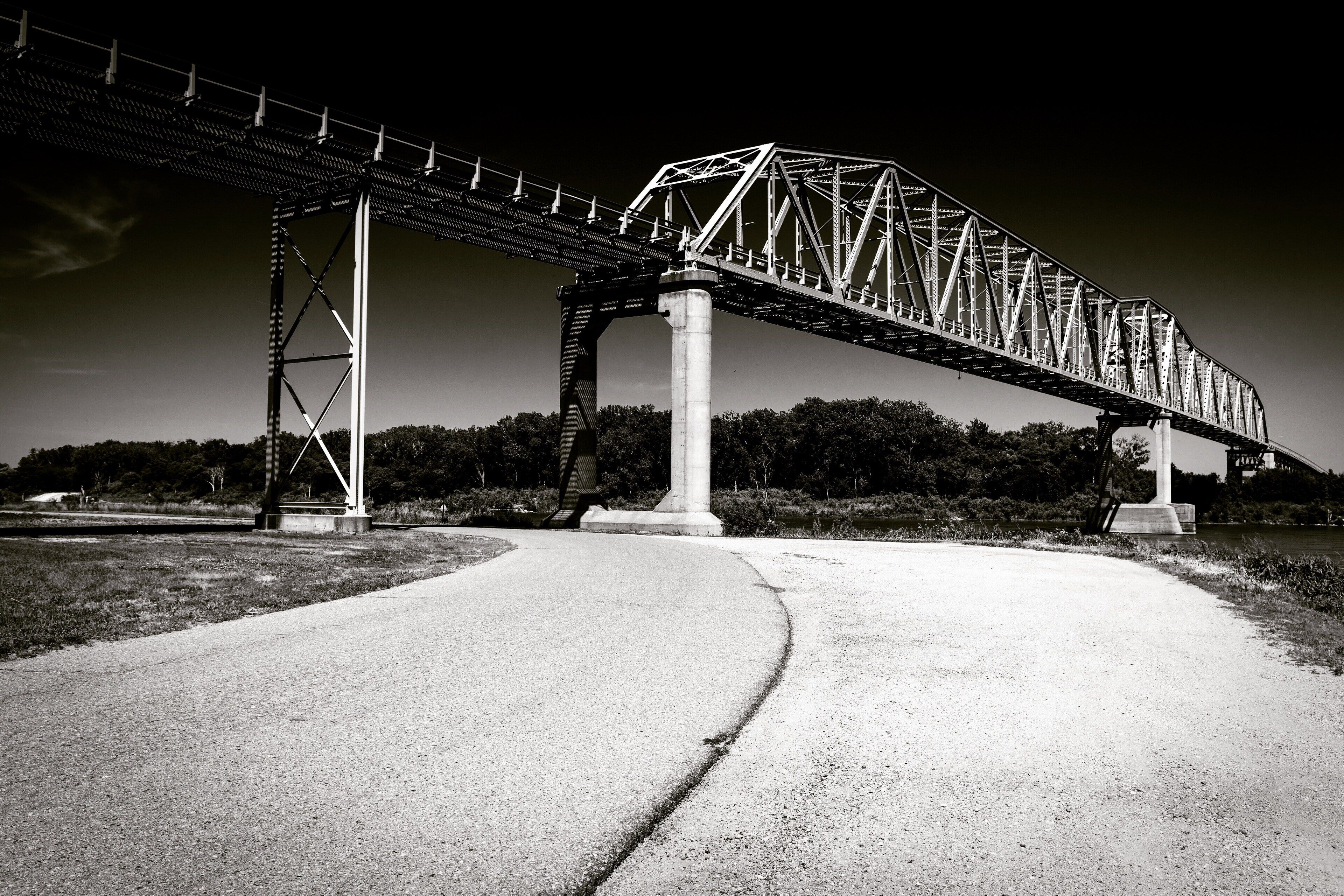 A steel bridge over a river with a concrete walkway leading to it.