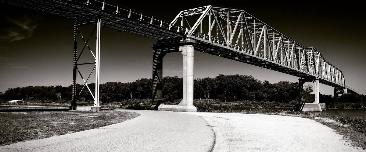 A steel bridge over a river with a concrete walkway leading to it.