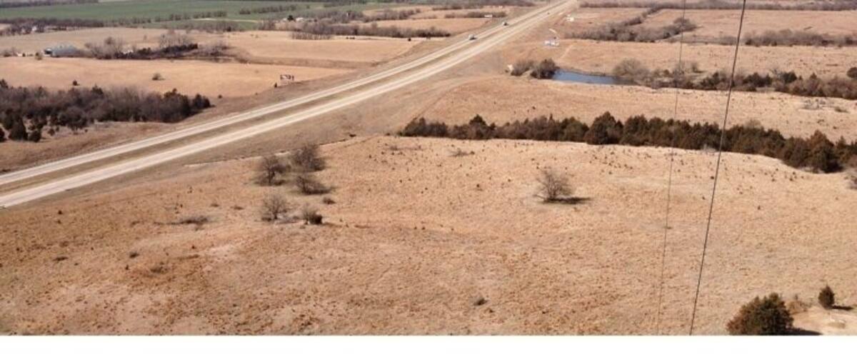 A long, straight road through a dry, open landscape with sparse vegetation and distant fields.
