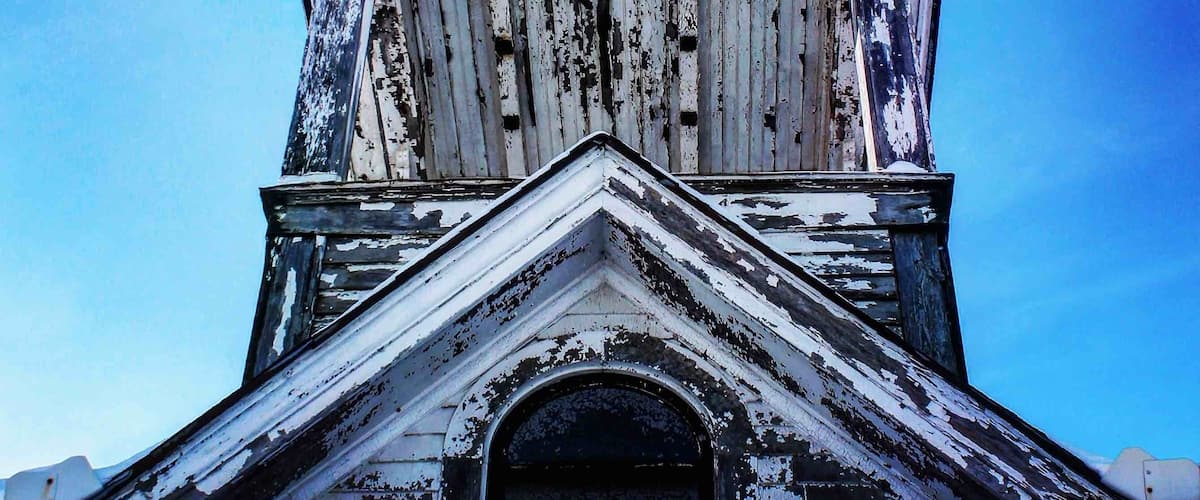 A weathered, white steeple with a pointed spire against a clear blue sky.