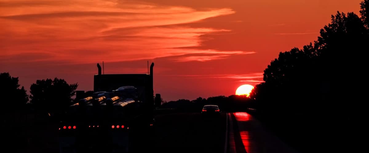A sunset over a highway with a truck and a car.