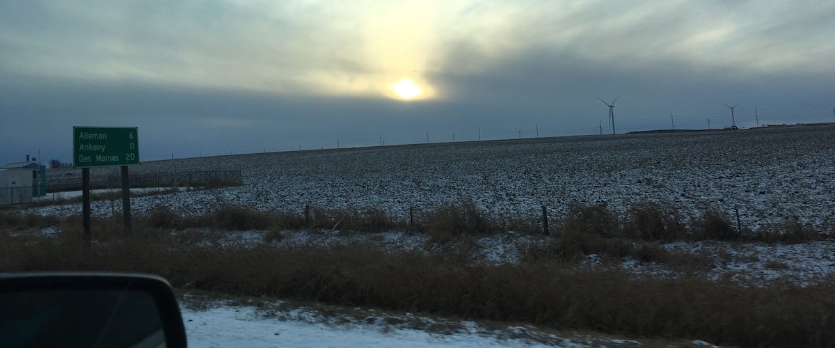 A road with a green highway sign indicating distances to Alleman, Ankeny, and Des Moines.