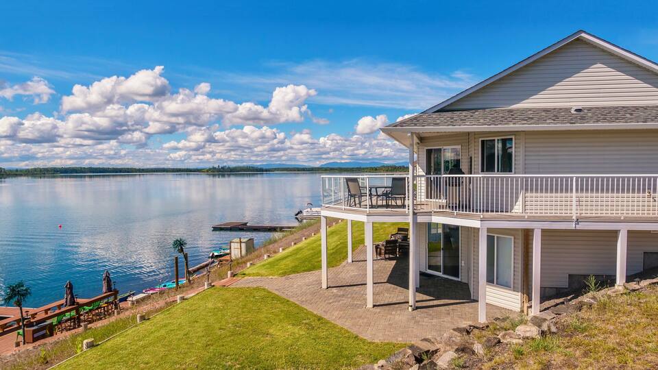 Wide angle view of a beautiful, large modern luxury summer holiday home, featuring sun decks, glass railings and large windows, set beside a small lake in central British Columbia, Canada.