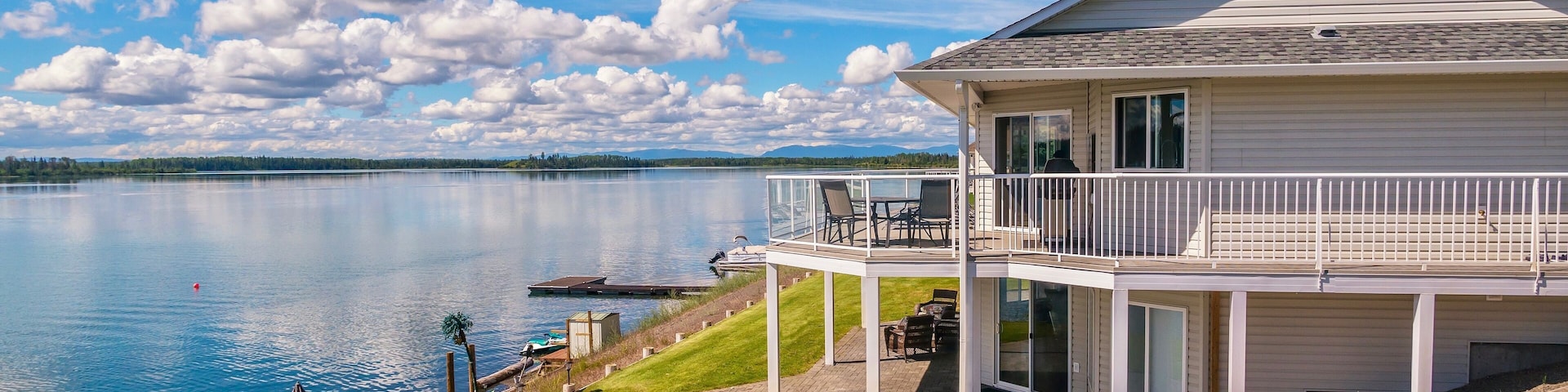 Wide angle view of a beautiful, large modern luxury summer holiday home, featuring sun decks, glass railings and large windows, set beside a small lake in central British Columbia, Canada.
